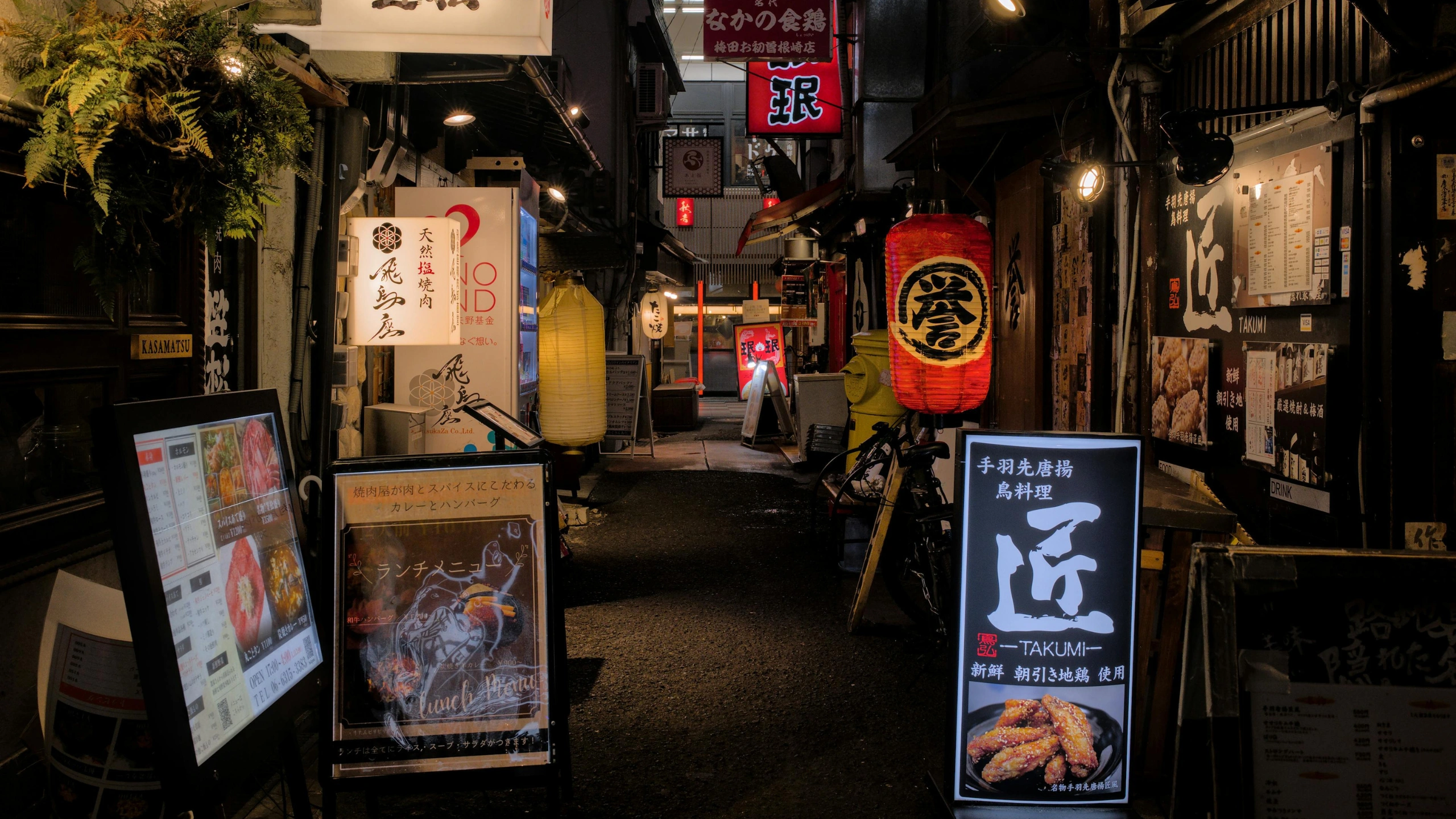 A narrow, lantern-lit alley in Japan lined with small eateries, colorful illuminated menus, and traditional signage creating a vibrant nighttime food street scene.